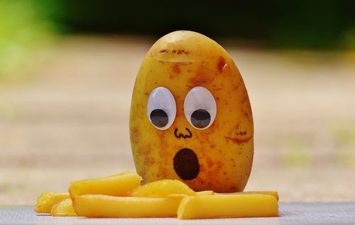 Kartoffel mit Gesicht schaut schockiert auf Pommes frites.